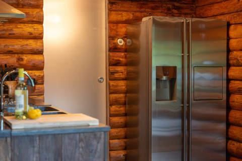 Küche in einer Blockhütte mit Edelstahlkühlschrank und Weinflasche bei Huys van de Boswachter, Sandberghe.