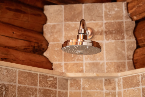 Cabezal de ducha en lodge rústico Huys van de Boswachter en Sandberghe, con azulejos y paredes de troncos.