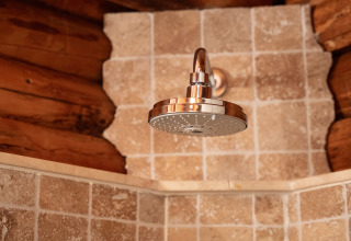 Cabezal de ducha en lodge rústico Huys van de Boswachter en Sandberghe, con azulejos y paredes de troncos.