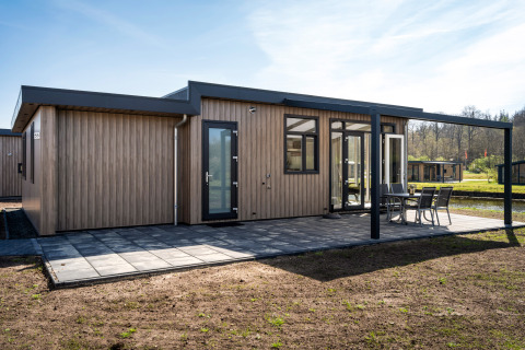 Lodge Zandduin Deluxe moderne avec façade en bois, grande terrasse et mobilier de jardin dans un cadre paisible.