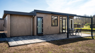 Moderne Zandduin Deluxe lodge met houten gevel, groot terras en tuinmeubelen in een rustige omgeving.