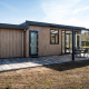 Moderne Zandduin Deluxe-lodge med træfacade, stor terrasse og havemøbler i naturskønne omgivelser.