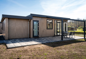 Moderne Zandduin Deluxe lodge met houten gevel, ruim terras en tuinset in een groene en rustige omgeving.