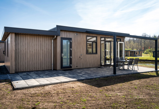 Moderne Zandduin Deluxe lodge met houten gevel, groot terras en tuinmeubelen in een rustige omgeving.