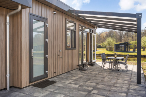 Moderne Zandduin Deluxe lodge bij De Tien Heugten in Nederland, met overdekt terras en zitje buiten.