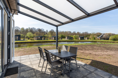Overdekt terras van Zandduin Deluxe lodge in De Tien Heugten met zicht op vijver en chalets in de natuur.