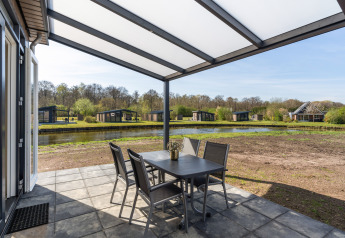 Overdekt terras bij Zandduin Deluxe lodge in De Tien Heugten met uitzicht op het meer en vakantiewoningen.