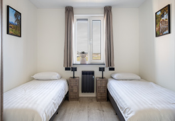Twee eenpersoonsbedden in een lichte, eenvoudige kamer met raam, schilderijen en nachtkastjes in Zandduin Deluxe, Nederland.