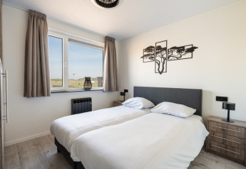 Modern bedroom at Zandduin Deluxe lodge in De Tien Heugten, Netherlands, featuring twin beds and wood art.