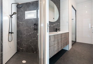 Moderne badkamer in Zandduin Deluxe-lodge bij De Tien Heugten met douche, wastafel en spiegel.