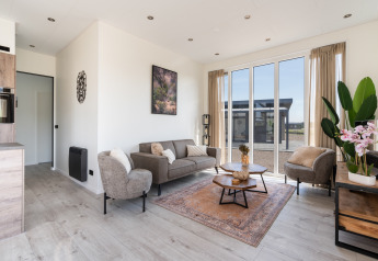 Bright, modern living room at Zandduin Deluxe, De Tien Heugten, with large windows, neutral tones and plants.