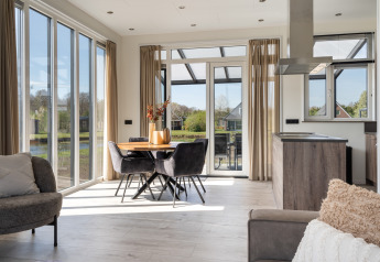 Bright, modern living and dining area in Zandduin Deluxe lodge at De Tien Heugten, Netherlands, with large windows.