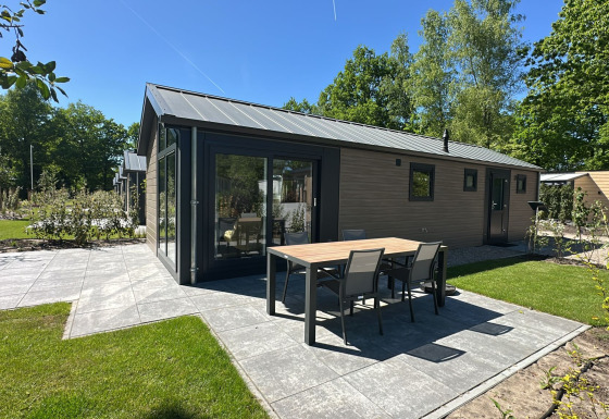 Moderne lodge met tuintafel en stoelen op het terras, omringd door gras en groene bomen.