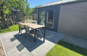 Terrasse am Lodge mit Tisch und vier Stühlen auf Fliesen, angrenzend an Rasen und moderne Fassade.