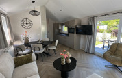 Modernes Lodge-Wohnzimmer mit großen Fenstern, Esstisch, gemütlicher Sitzecke, Küche und Gartenblick.