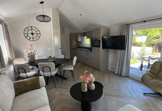 Moderne lodge living met grote ramen, eetruimte, zitgedeelte, open keuken en zicht op de tuin.