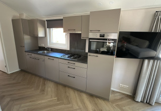 Moderne lodge keuken met grijze kasten, gaskookplaat, ingebouwde oven en tv aan de muur bij het raam.