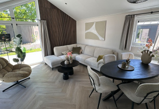 Moderne lodge woonkamer met grote ramen, lichte meubels, ronde tafel en zicht op de tuin.