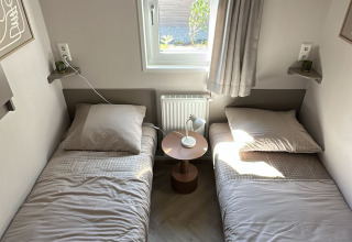 Twee eenpersoonsbedden met beige lakens en een nacht kastje onder een raam in een gezellige lodgekamer.