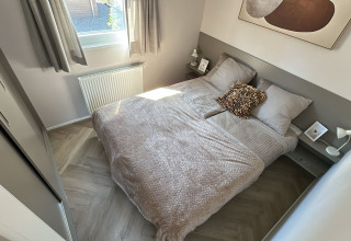 Lichte, gezellige slaapkamer in een lodge met tweepersoonsbed, nachtkastjes en groot raam.