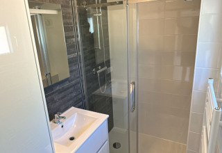 Moderne lodge badkamer met douche, donkere vloertegels, witte wastafel en een grote spiegel.