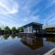 Moderne husbåd på vandet ved Marina Heeg i Holland, omgivet af blå himmel og frodige grønne træer.