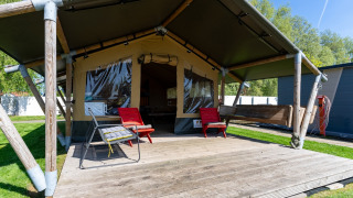 Tenda safari a Marina Heeg nei Paesi Bassi con terrazza in legno, sedie rosse e atmosfera rilassante.