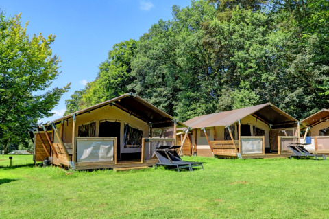 Tende safari di lusso con veranda in legno al Camping La Colline, Belgio Lussemburgo, immerse nel verde.