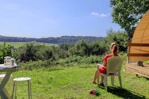 Frau sitzt auf einem Stuhl vor einem Zelt und genießt den Ausblick bei Camping La Colline in Belgien.