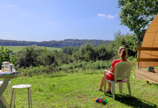 Woman sitting in a chair outside a tent enjoying scenic green views at Camping La Colline, Belgium.