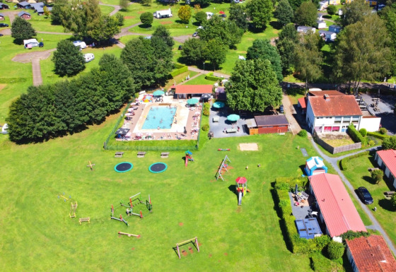 Vista aerea di Camping La Colline in Belgio con piscina, area giochi, prati verdi e bungalow vacanza.
