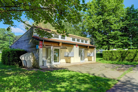 Gemeinschaftsgebäude im Camping La Colline, umgeben von Grünflächen und Bäumen in Luxemburg, Belgien.