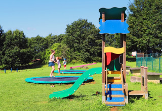Children and adults enjoy trampolines and a playground on the grassy field at Camping La Colline, Belgium.
