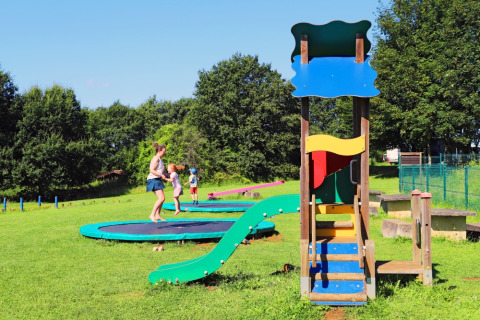 Børn og voksne leger på trampoliner og legeplads i grønt område på Camping La Colline, Belgien.