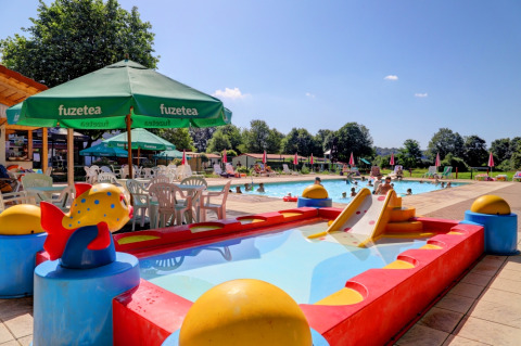 Außenpoolbereich im Camping La Colline, Belgien, mit Kinderbecken, Rutsche und Sonnenschirmen.