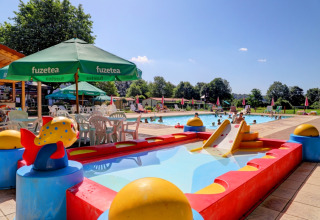 Outdoor pool area at Camping La Colline, Belgium, featuring a kids' pool, slide, and sun umbrellas.