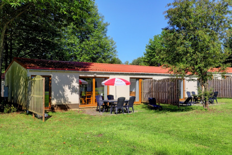 Ferienhaus im Camping La Colline, Belgien Luxemburg, mit Gartenmöbeln und Sonnenschirm auf Rasenfläche.