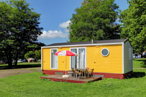 Yellow mobile home at Camping La Colline in Belgium Luxembourg, surrounded by green grass and trees.