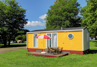 Yellow mobile home at Camping La Colline in Belgium Luxembourg, surrounded by green grass and trees.