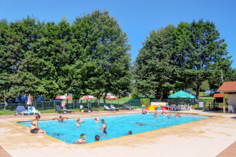 Familien genießen das Schwimmbecken im Camping La Colline in Belgien, umgeben von Bäumen und Liegestühlen.