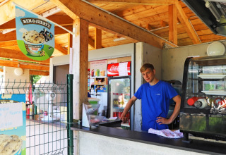 Young man at outdoor ice cream counter at Camping La Colline, Belgium, with Ben & Jerry's sign.