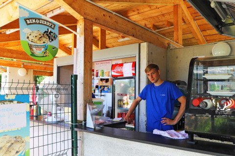 Joven en puesto de helados al aire libre en Camping La Colline, Bélgica, con cartel de Ben & Jerry's.