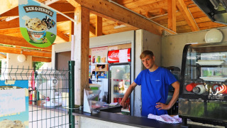 Joven en puesto de helados al aire libre en Camping La Colline, Bélgica, con cartel de Ben & Jerry's.