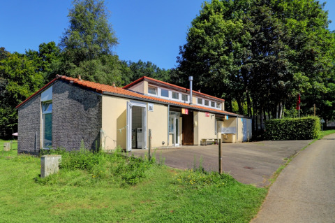 Foto eines Gemeinschaftsgebäudes auf Camping La Colline in Belgien-Luxemburg mit viel Grün und Bäumen.