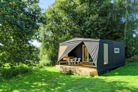A modern black tent-style holiday cabin with deck, set in lush greenery at Camping La Colline, Belgium.