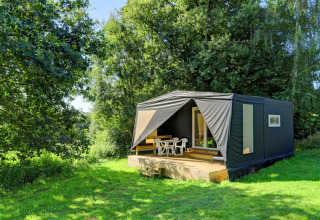 A modern black tent-style holiday cabin with deck, set in lush greenery at Camping La Colline, Belgium.