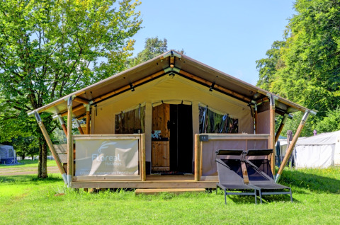 Tenda glamping al Camping La Colline, Belgio Lussemburgo, con sdraio e ambientazione verde lussureggiante.