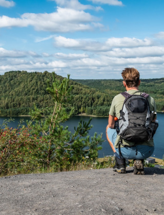 Homme avec sac à dos admire un lac et des collines boisées dans un parc de vacances avec glamping.