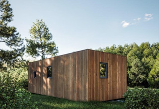 Modern wooden cabin with simple, boxy architecture in lush Hameau de l'Ourthe holiday park, Belgium.
