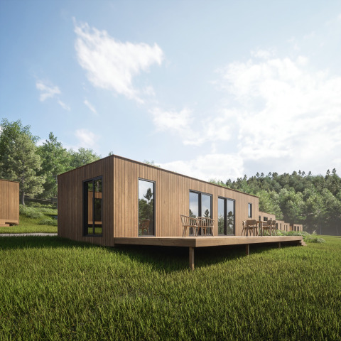 Træhytte med terrasse i sollys på Hameau de l'Ourthe feriepark, omgivet af grønt græs og skov.